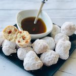 Black plate of Beignets with white bowl of maple syrup