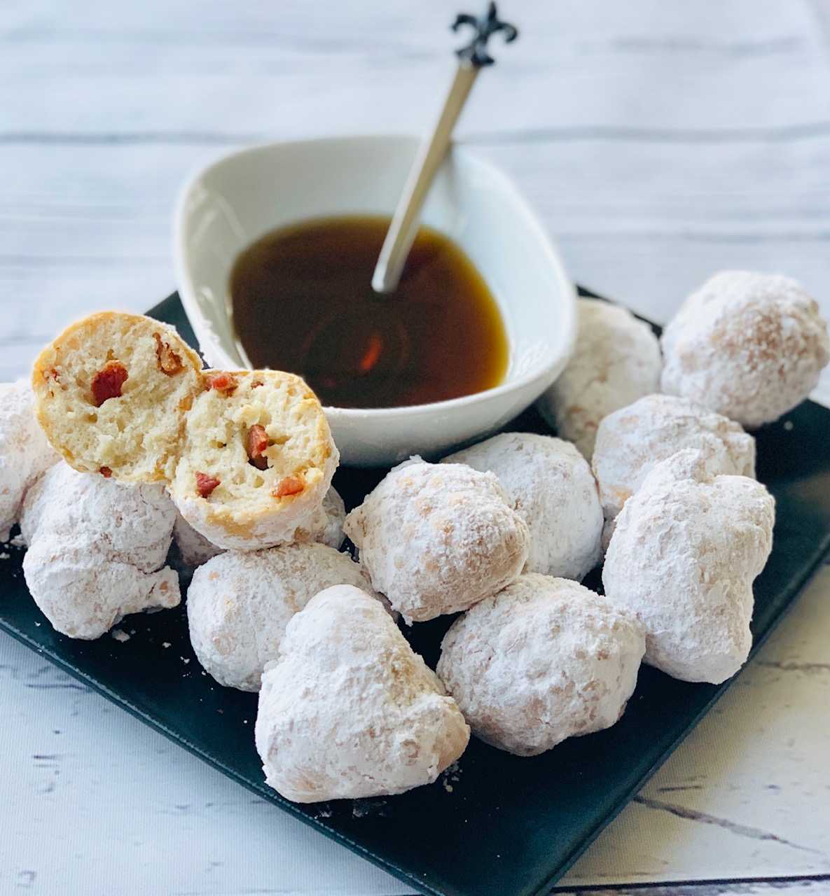 Black plate of Beignets with white bowl of maple syrup