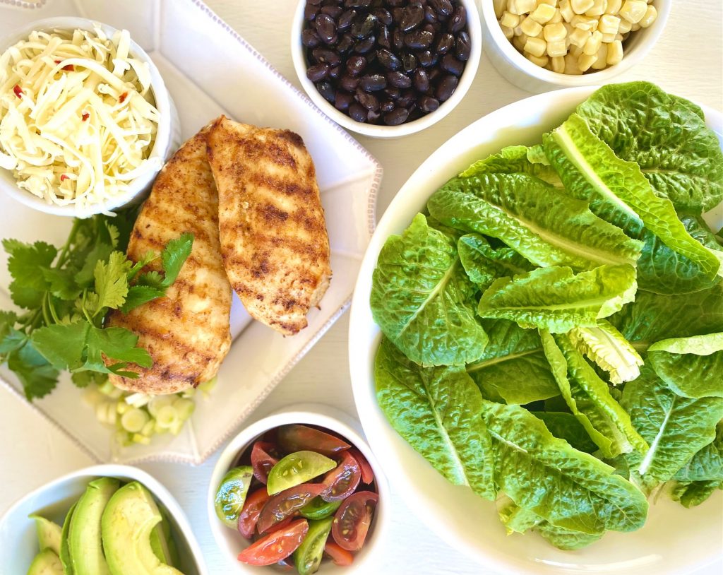 bowls of Romaine, chicken, tomatoes, corn, black beans, avocado, cheese and cilantro