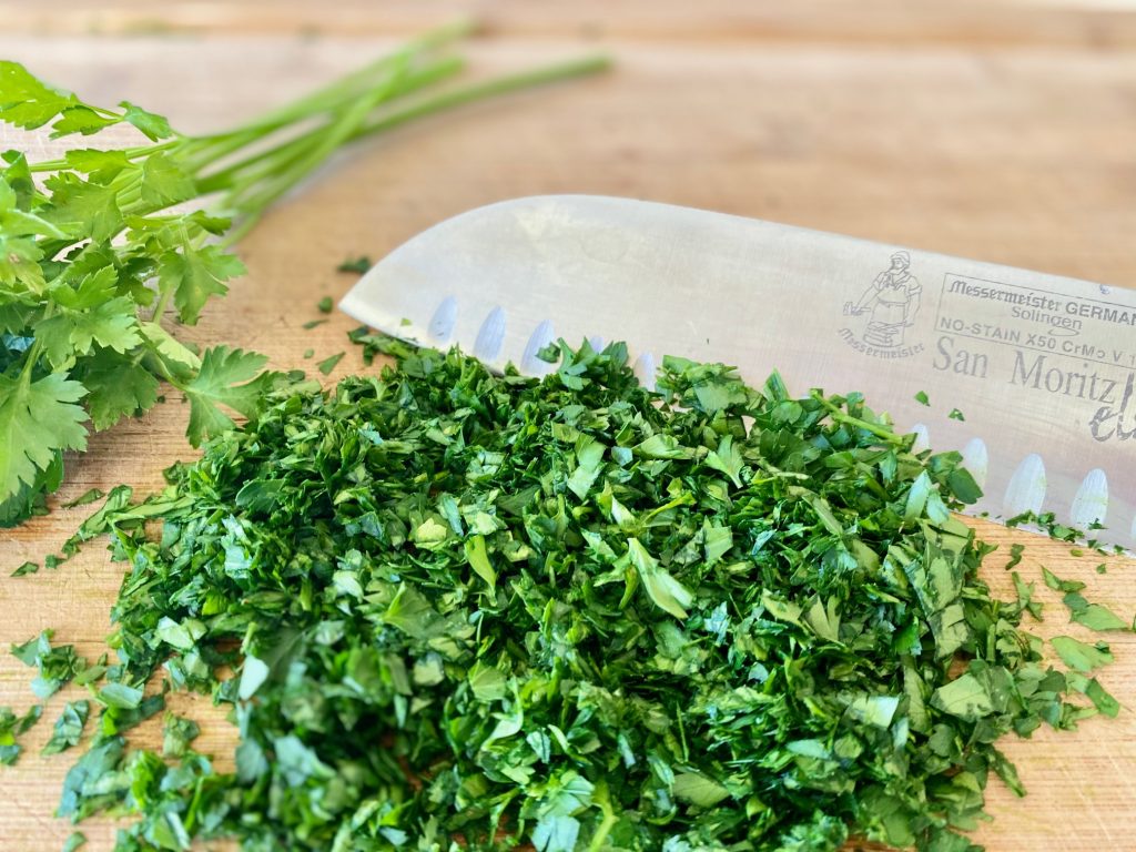 Chopped parsley and cilantro on a cutting board with a knife