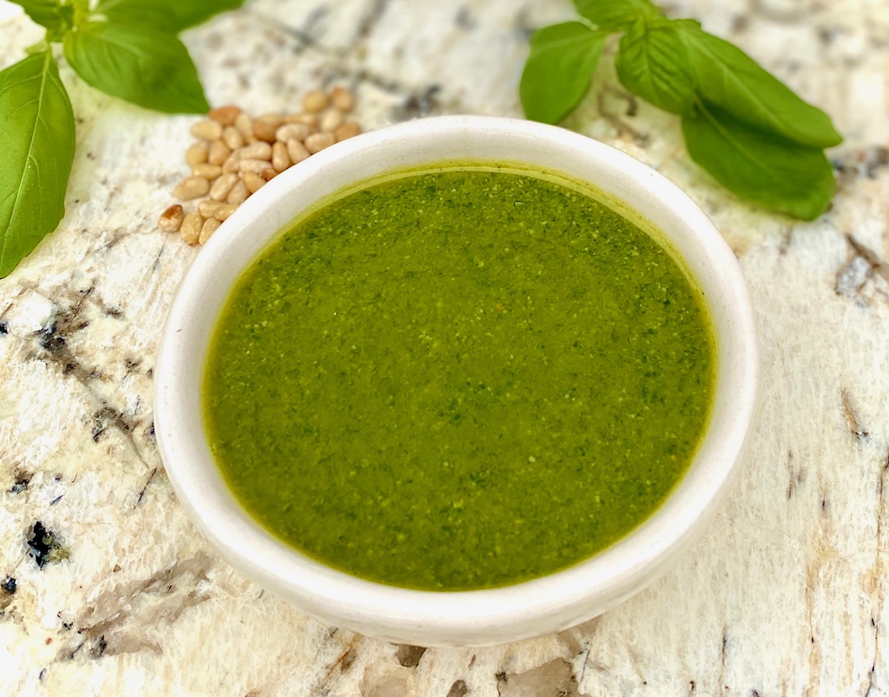 white bowl of pesto with pine nuts and basil