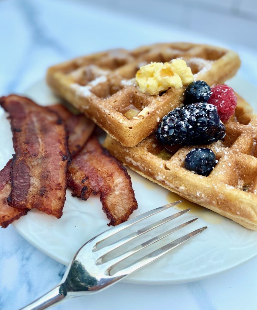 bacon, waffles and fruit on white plate with fork