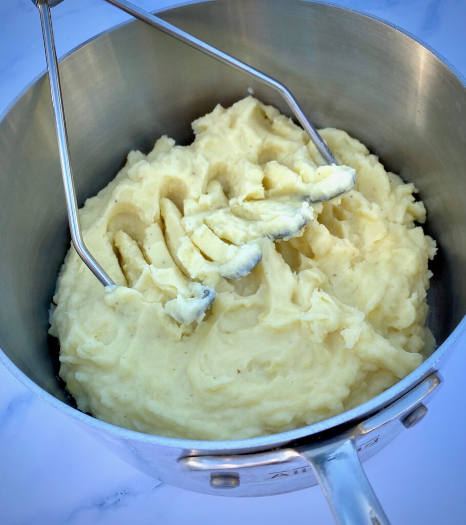 Mashing potatoes with a masher in a silver pan