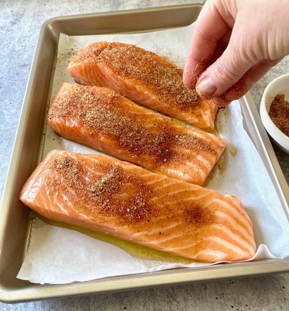 Sprinkling 3 salmon filets with seasoning