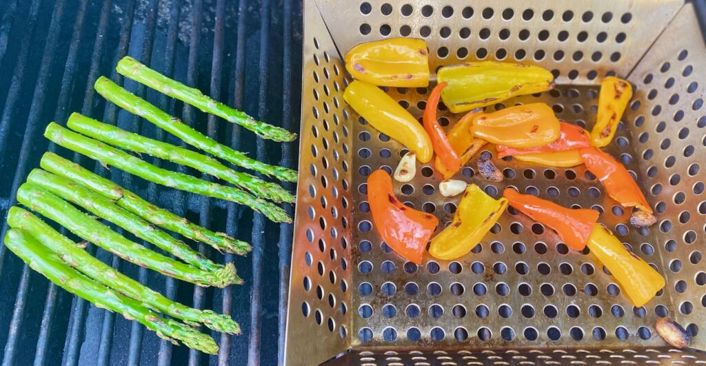 peppers in a grill basket and asparagus on grill grates