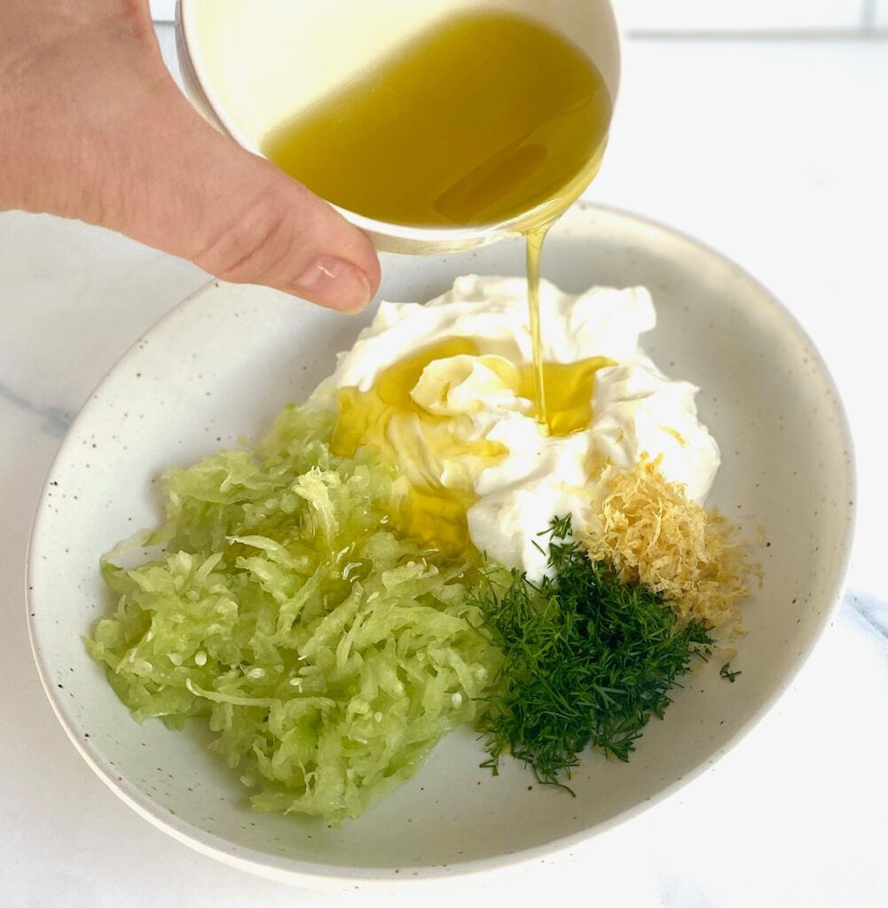 Pouring olive oil on tzatziki ingredients