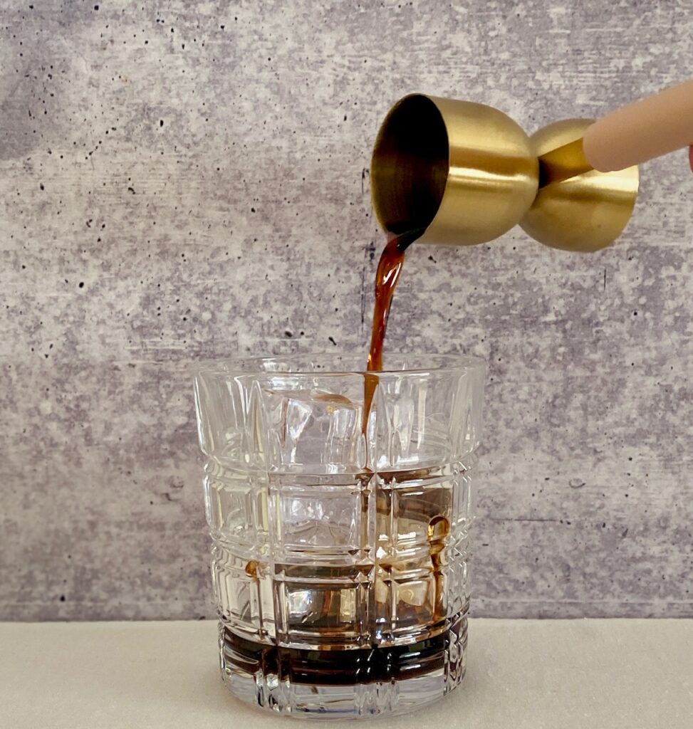 pouring kahlua coffee liqueur into a glass with ice