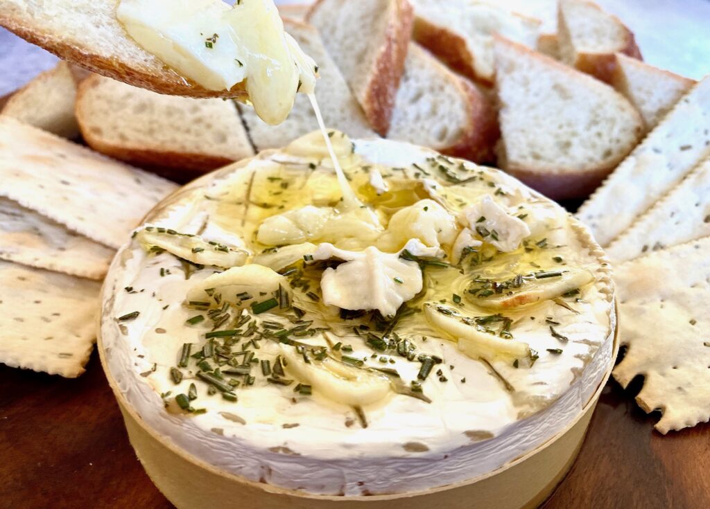 a round of cheesey melted brie with bread and crackers