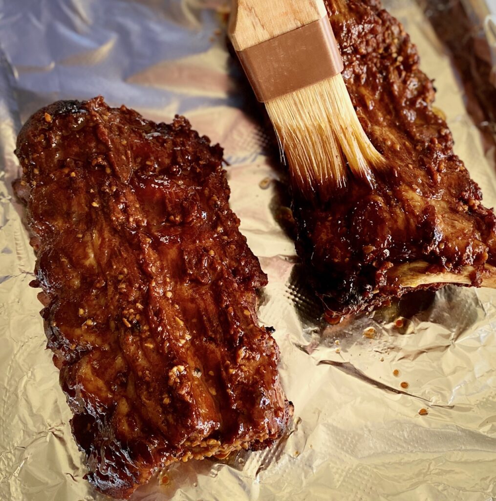 brushing bbq sauce on rack of baby backs