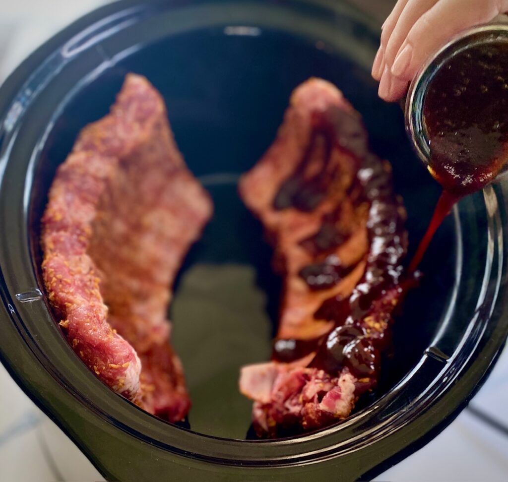 pouring bbq sauce on ribs in crockpot