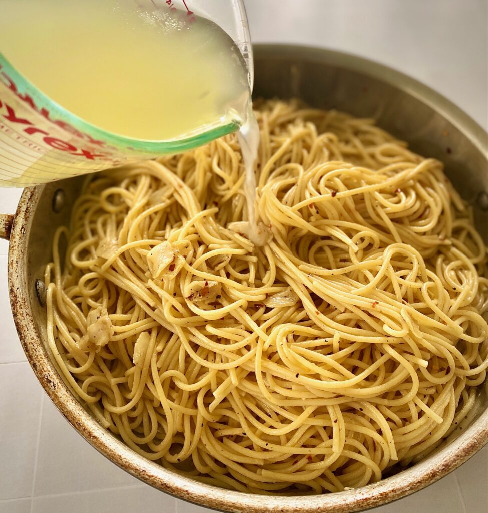 adding hot pasta water to pan of spaghetti