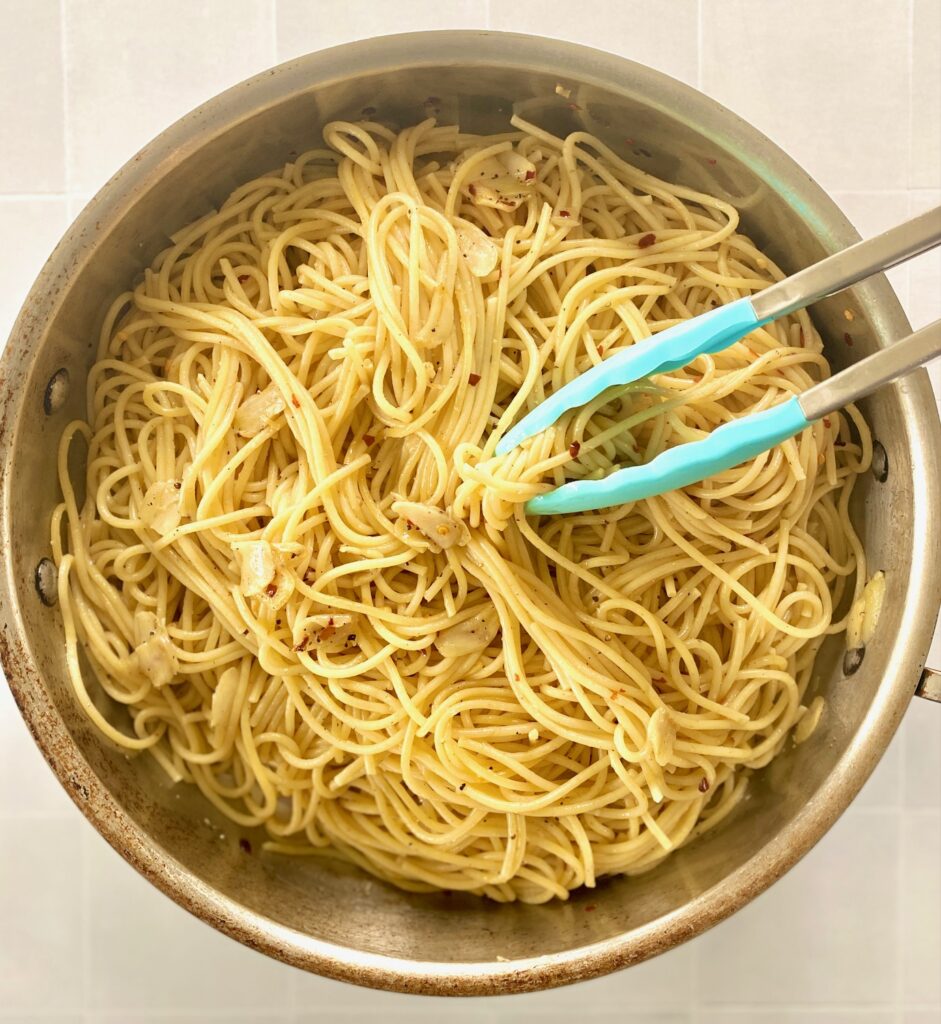 pan of garlic and red pepper pasta with tongs