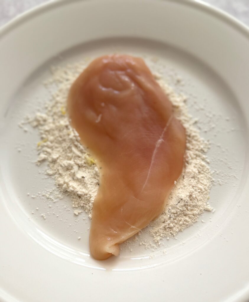chicken breast with flour on a white plate