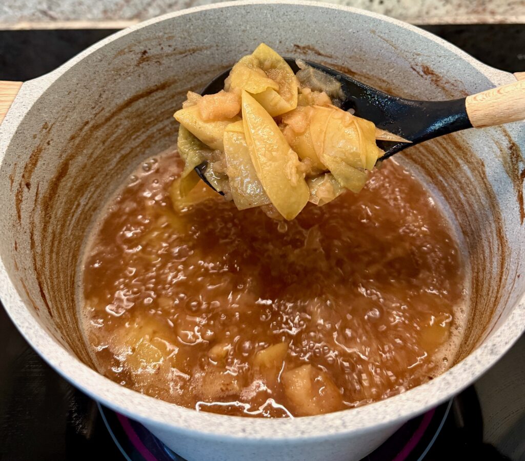 apples cooked for cider on a spoon in a gray pot