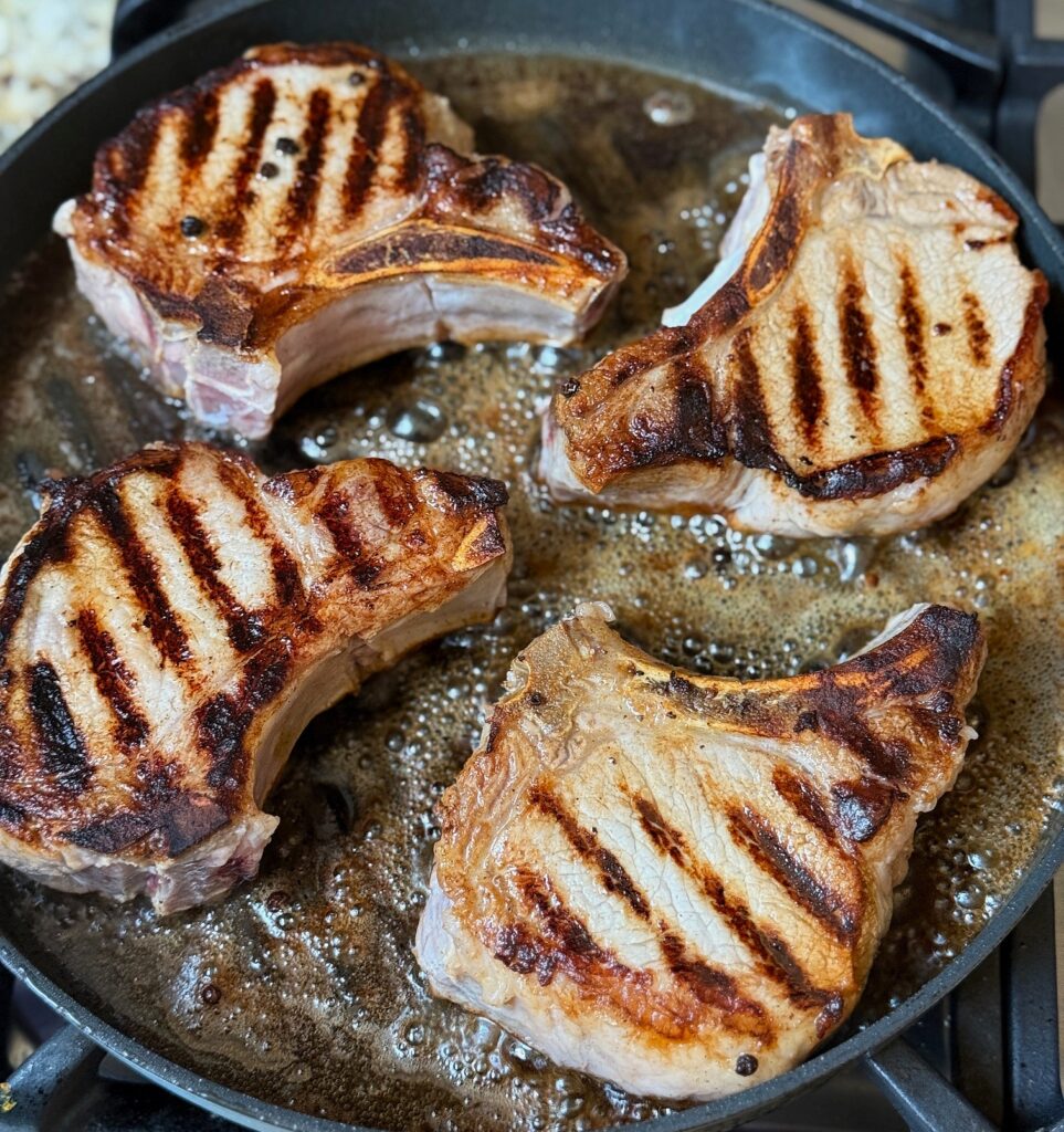 4 pork chops cooking in a black pan